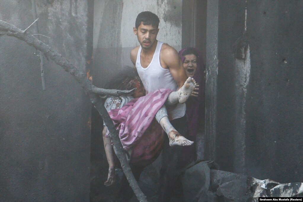 Një burrë mban një vajzë palestineze të plagosur ndërsa një grua reagon duke qarë mes muresh të nxira nga tymi si pasojë e  sulmeve izraelite në Khan Younis, në Rripin e Gazës, 11 tetor 2023.