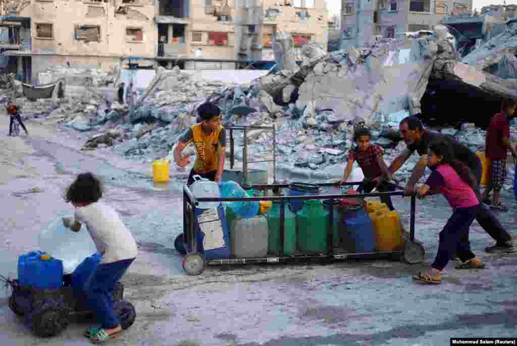 Një burrë palestinez dhe fëmijët shtyjnë një karrocë me enë të mbushura me ujë, në Han Junis, 3 qershor 2024.