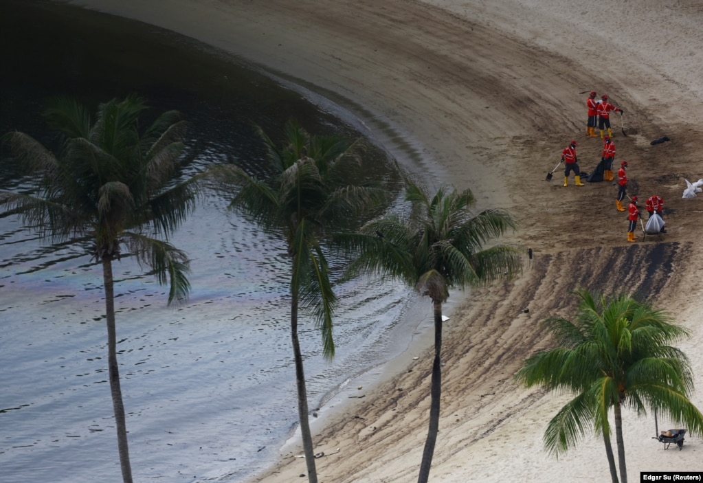 Punëtorët duke pastruar shtresat e naftës në plazhin Siloso në Sentosa, Singapor, 18 qershor 2024.