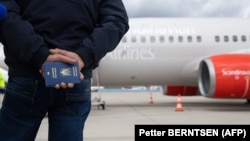 Мужчина держит украинские паспорта для себя и своей жены, ожидая на взлетно-посадочной полосе рядом с самолетом медицинской эвакуации (Medevac) в аэропорту Кельн/Бонн в Германии, 23 марта 2023 года