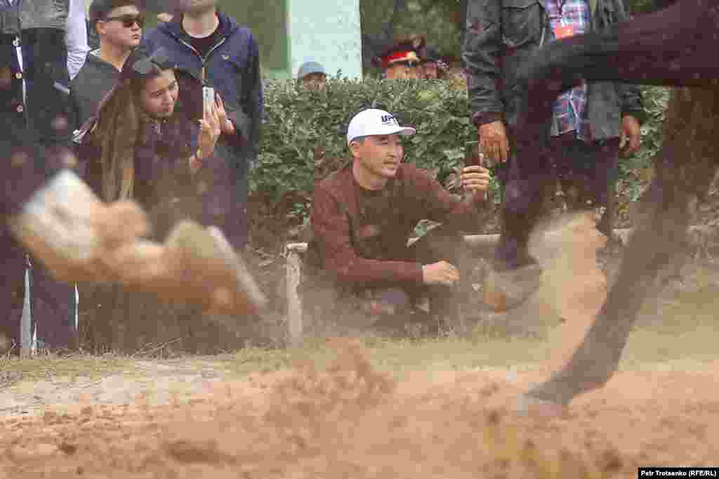 As horses thunder down the track, spectators capture the races on their mobile phones.