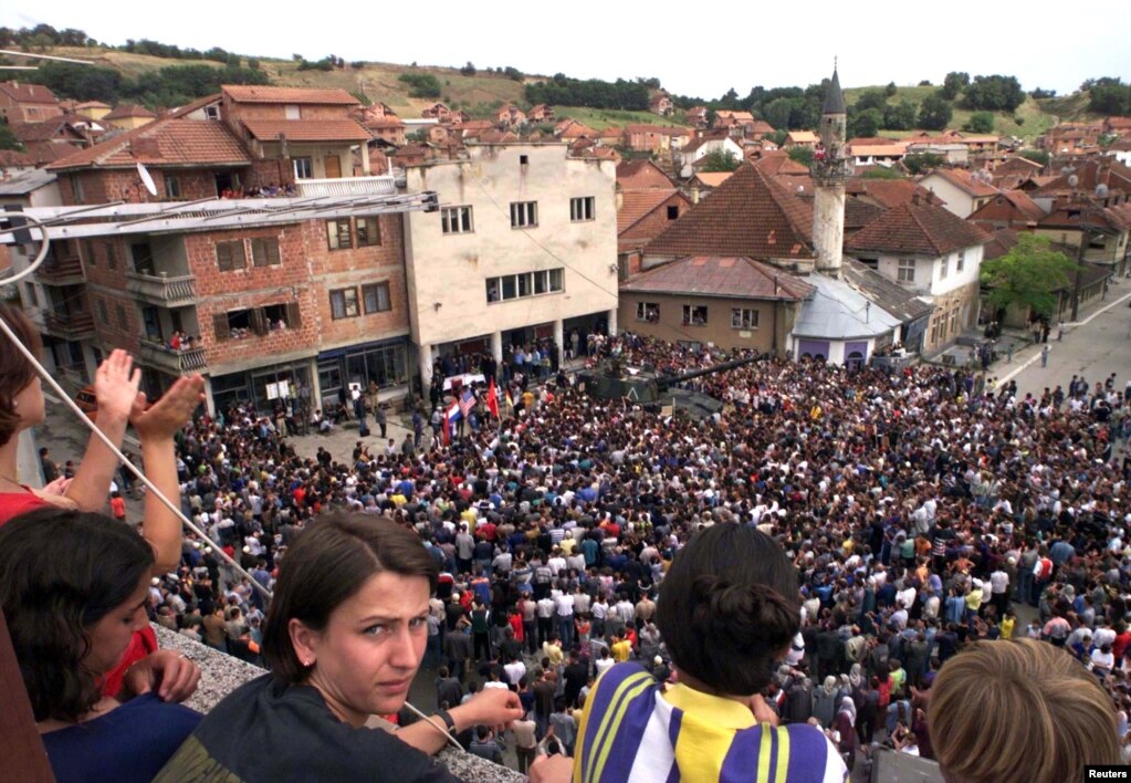 Rahovec 10 korrik 1999: Mijëra qytetarë kishin dalë këtë ditë në qendër të qytetit në Rahovec në ditën e katërt të protestës kundër një dislokimi të mundshëm të trupave paqeruajtëse ruse. Qytetarët shqiptarë të Rahovecit kishin protestuar për disa ditë duke thënë se paraushtarakët rusë kishin marrë pjesë në dhunën serbe kundër tyre.   6 qershor 2024: Përveçse është zvogëluar hapësira e sheshit, xhamia është rrënuar dhe ndërtuar një e re. Disa objekte që shihen para 25 vjetësh ende janë aty, vetëm se kanë pamje tjetër të jashtme. 