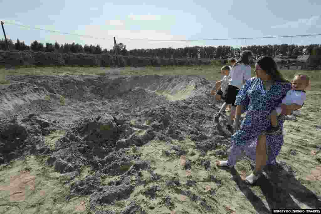 Locals view a bomb crater following a Russian missile strike in a village outside of Kyiv.