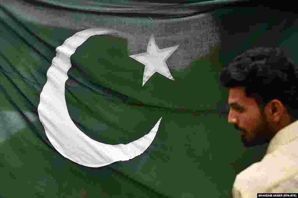 A man stands in front of the Pakistani national flag a day ahead of Independence Day celebrations in Karachi on August 13. Pakistan has been rocked by significant shocks over the past year, including floods that caused more than $30 billion in damage, political instability, and record-breaking inflation amid a worsening economic situation. &nbsp;