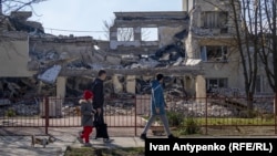 Locuitori ai orașului ucrainean Herson, trecând pe lângă clădirea distrusă de bombardamente a Academiei de Educație Continuă, martie 2024 