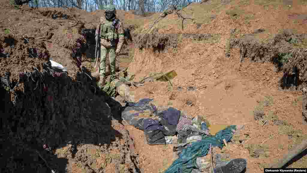 A Ukrainian soldier looks at the bodies of dead Russian soldiers in a trench.