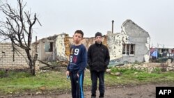 Хлопці стоять біля зруйнованої обстрілами будівлі в українському селі Новогригорівка Миколаївської області, 10 квітня 2023 року