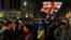 Мъж, увит в украинското знаме, издига флага на Грузия и знамето на ЕС по време на протеста в Тбилиси, Грузия, вечерта на 9 март 2023 г.