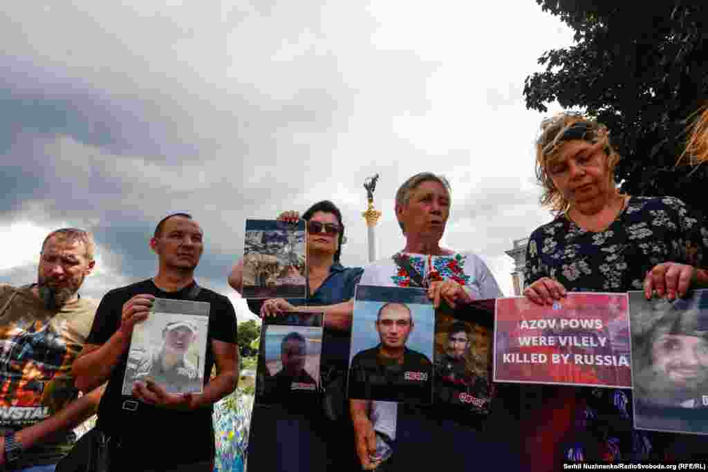 Поруч із фотографією військового жінка тримає плакат із написом: &laquo;Полонені азовці були підступно вбиті Росією&raquo; (переклад з англійської)