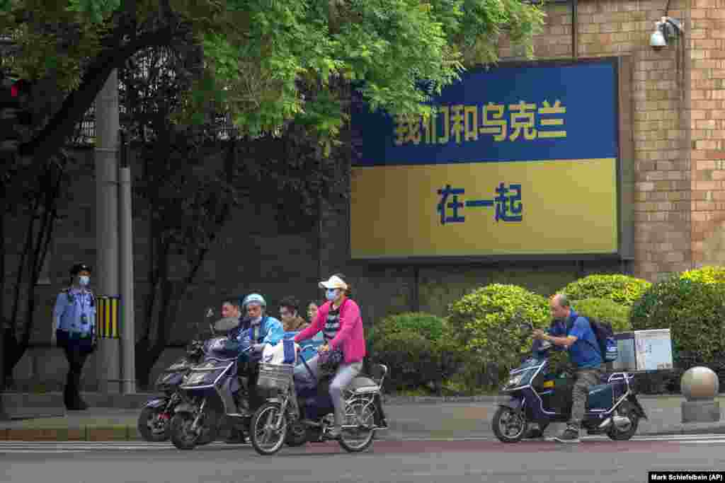 A policeman patrols as people riding bicycles and scooters wait to cross an intersection near a sign reading &quot;We stand with Ukraine&quot; outside the Canadian Embassy in Beijing.