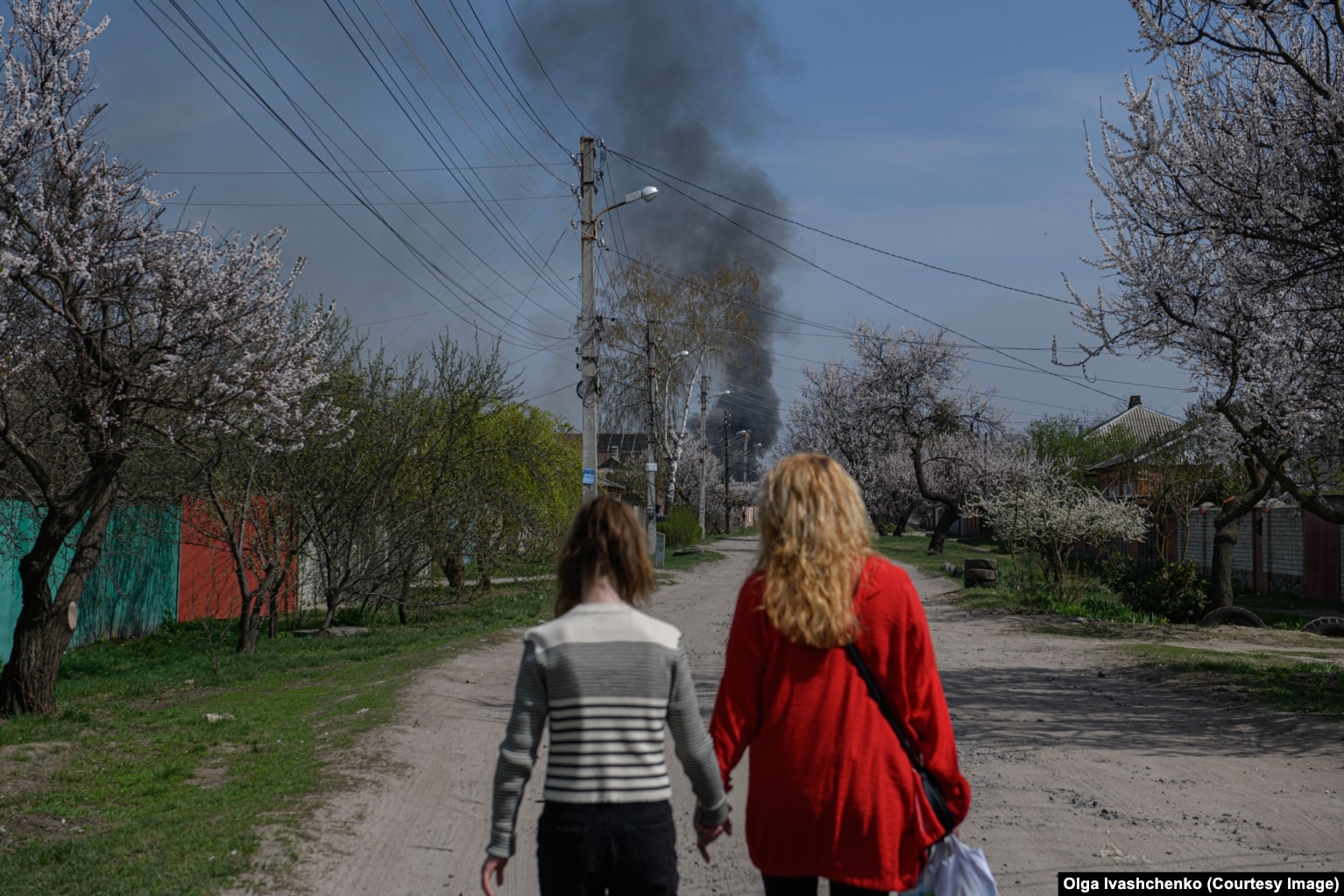 Një grua dhe një vajzë duke ecur nëpër një rrugë në periferi të Harkivit ndërsa para tyre shihet tymi që ngrihet në qiell nga një zjarr, më 9 prill.