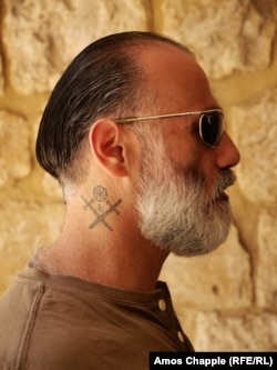 Bedig Giragosian, a Jerusalem Armenian, shows his tattoo of the traditional Armenian symbol of eternity above two crossed swords.