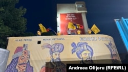 Susținători ai partidului naționalist-suveranist AUR flutură steaguri ale României pe o clădire acoperită cu un banner care prezintă figuri istorice medievale la sediul partidului după exit-pollurile de la alegerile din 9 iunie 2024.