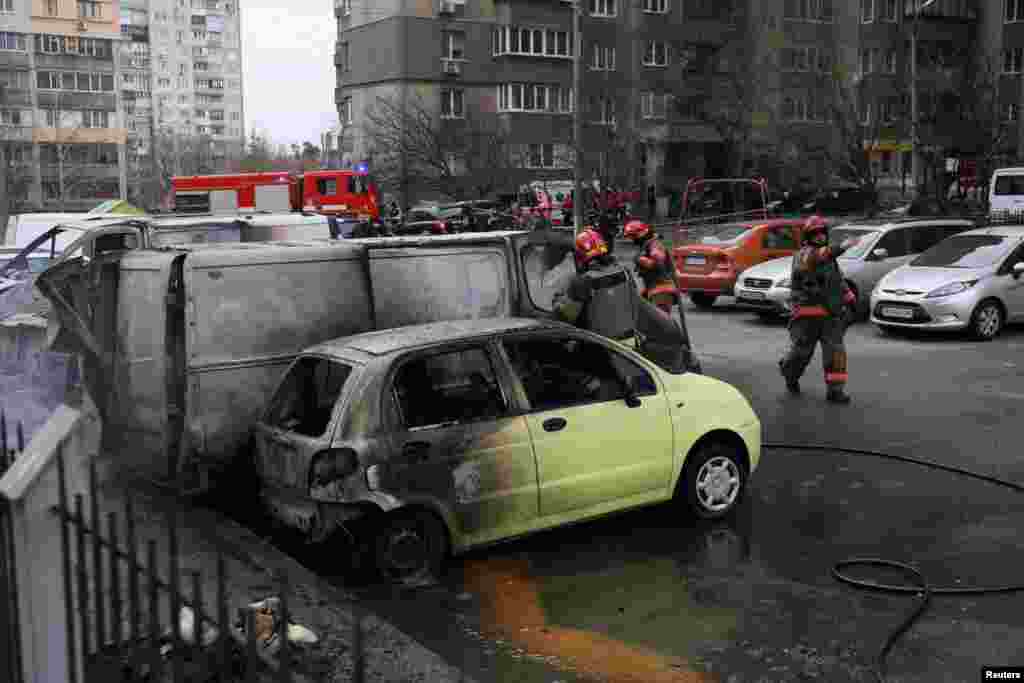 Radnici hitnih službi gase požar na vozilima na mjestu ruskog napada u Kijevu.