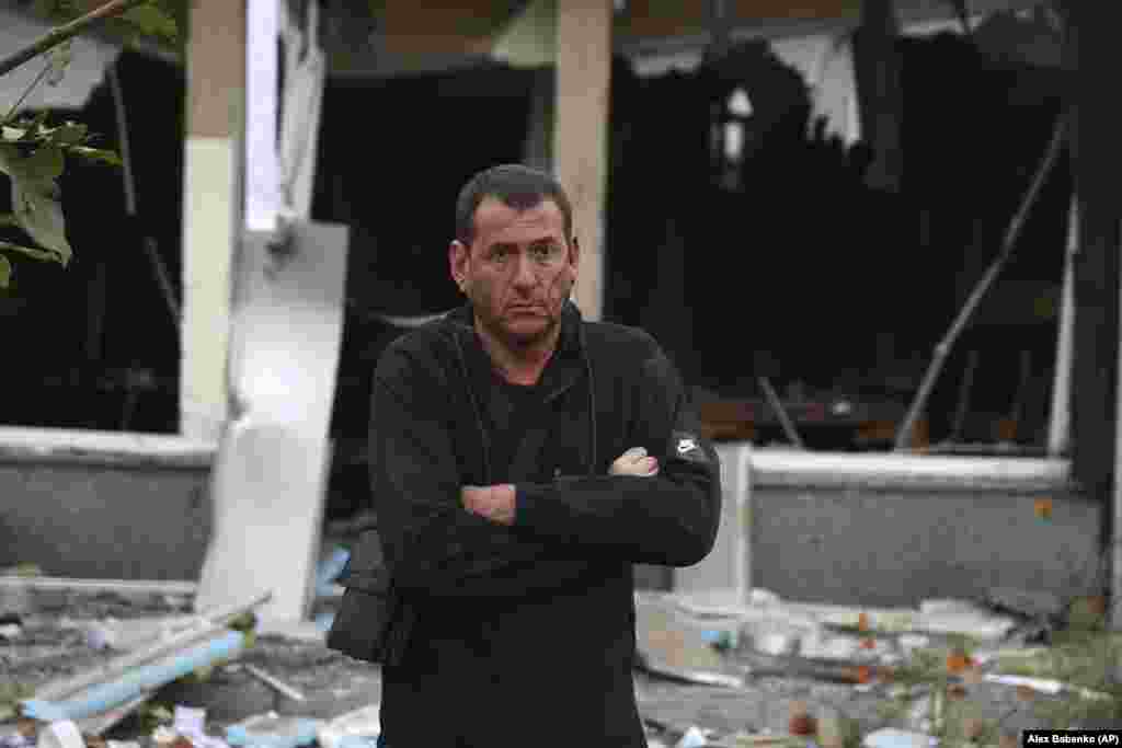 An injured man stands in front of a destroyed building.