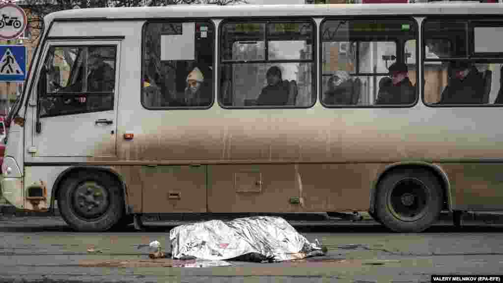 Putnici u autobusu gledaju pokriveno tijelo mrtvo žene nakon granatiranja u centru Donjecka, u Ukrajini pod ruskom kontrolom.