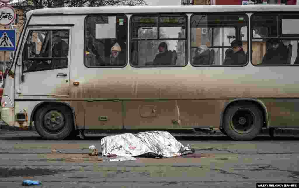 Commuters on a bus look at the covered body of a woman in the aftermath of shelling in downtown Donetsk, in Russian-controlled Ukraine.