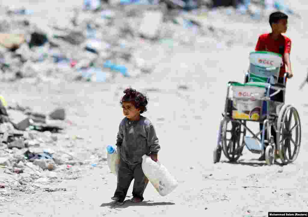 Një vajzë palestineze mban shishe plastike për të marrë ujë ndërsa ecën pranë rrënojave të shtëpive që u shkatërruan nga sulmet izraelite, në mes të konfliktit të vazhdueshëm midis Izraelit dhe Hamasit - i shpallur organizatë terroriste nga SHBA-ja dhe BE-ja. Han Junis, Rripi i Gazës, 22 maj 2024.