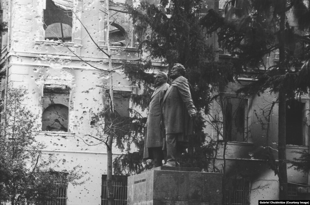 Una statua degli scrittori georgiani e delle figure nazionali Ilia Chavchavadze e Akaki Tsereteli davanti a un edificio sventrato vicino al parlamento georgiano