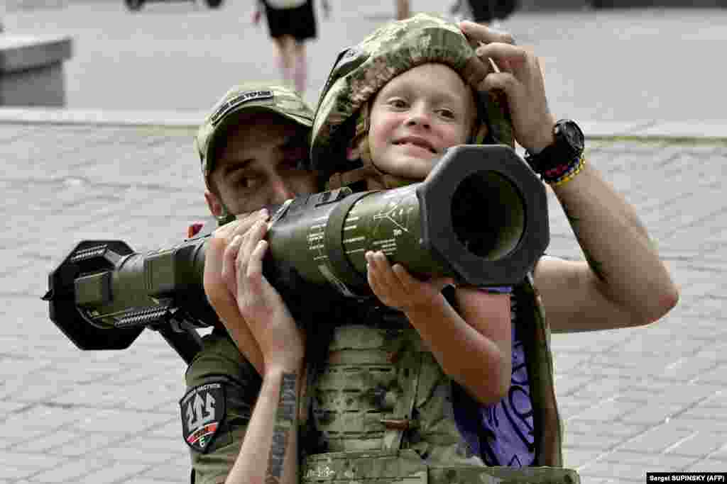 A Ukrainian soldier helps a boy wearing body armor hold an AT4 Swedish man-portable anti-tank weapon in the center of Kyiv on August 10.
