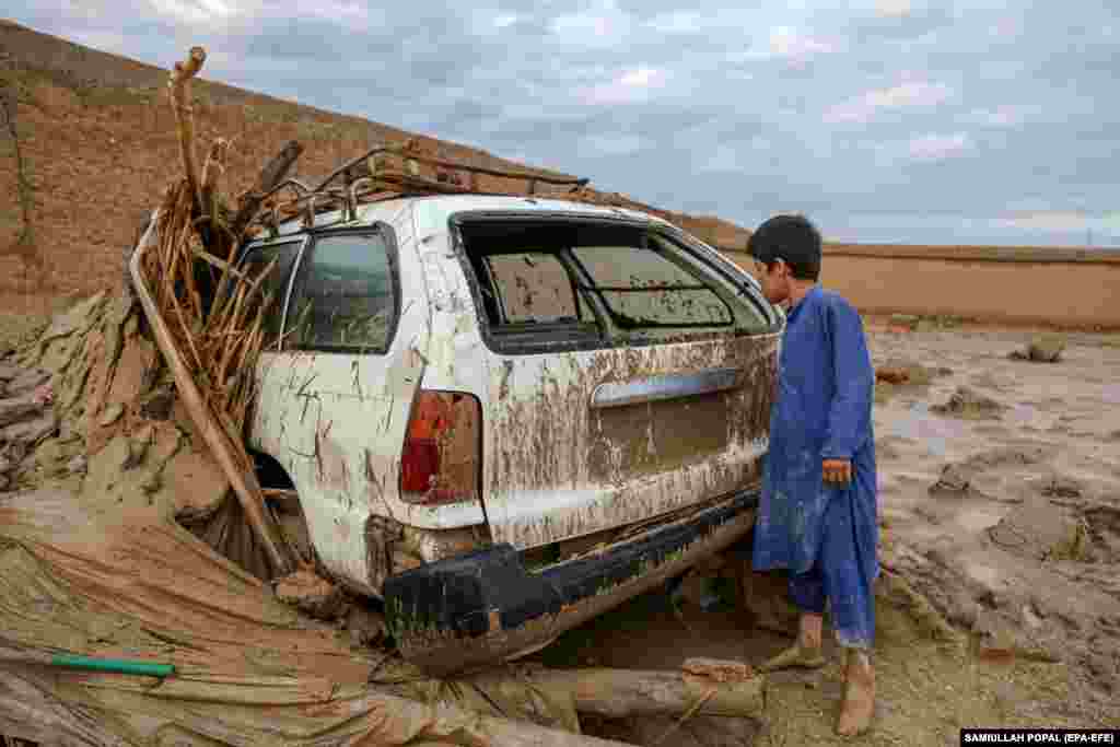 An Afghan boy surveys a vehicle stuck in a flooded area after flash floods in the village of Shahrak Muhajireen.