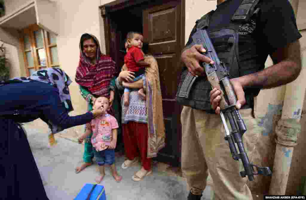 Police escort health workers as they administer a polio vaccine to a child in Karachi, Pakistan.