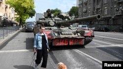 O femeie cu un câine trece pe lângă un tanc în timp ce luptătorii grupului Wagner sunt desfășurați pe o stradă în apropierea cartierului general al Districtului Militar Sudic din orașul Rostov-on-Don, Rusia, pe 24 iunie 2023. 