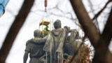 Two workers suspended above the lead figures of the partially dismantled Monument To The Soviet Army on the morning of December 13.<br />
<br />
The topmost portion of the monument -- depicting a Soviet soldier&rsquo;s outstretched right arm and submachine gun -- was cut off the night before.<br />
&nbsp;
