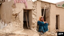 An Afghan woman sits in front of a damaged house after flash floods hit the Madrasa village in Ghor Province on May 24.