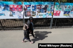 People walk past a board with official campaign posters of the upcoming parliamentary and regional elections in Almaty, but no "experiments" will take place there soon.