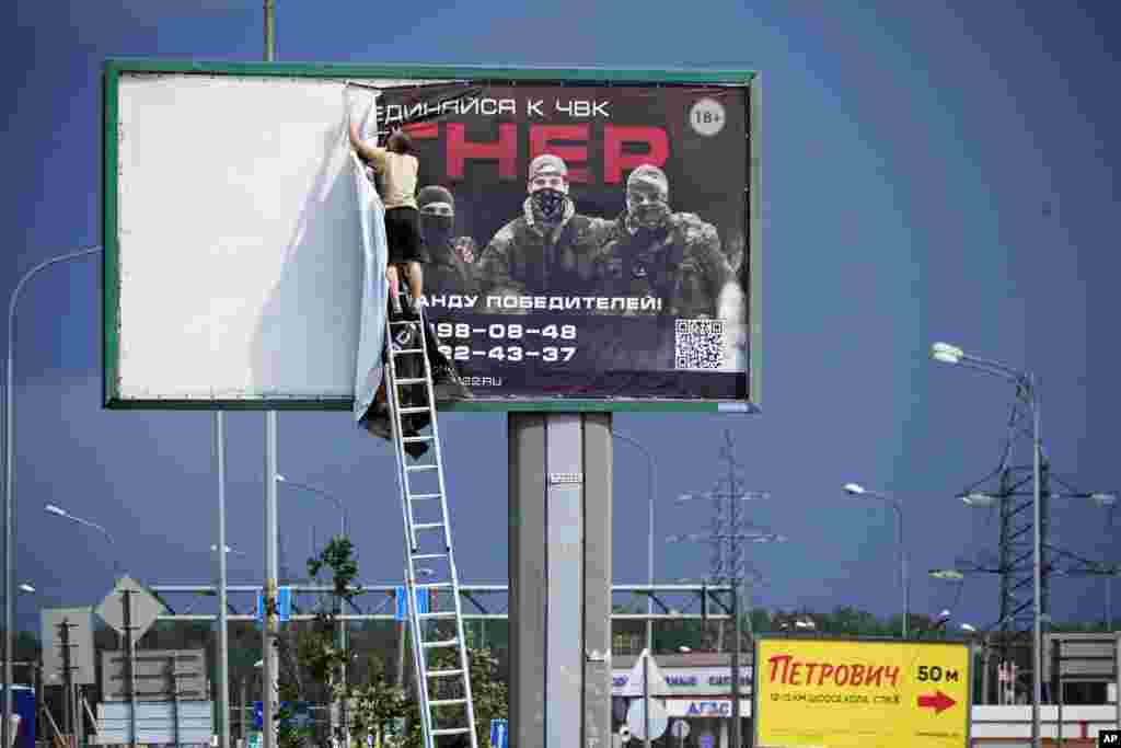A man pulls down a billboard that was recruiting men into the Wagner group on June 24. The billboard stood alongside a highway on the outskirts of St. Petersburg.&nbsp;