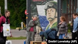 Женщины продают подержанные и новые товары на уличном рынке рядом с рекламным щитом для призыва в армию. Санкт-Петербург, Россия, 8 июня 2023 года