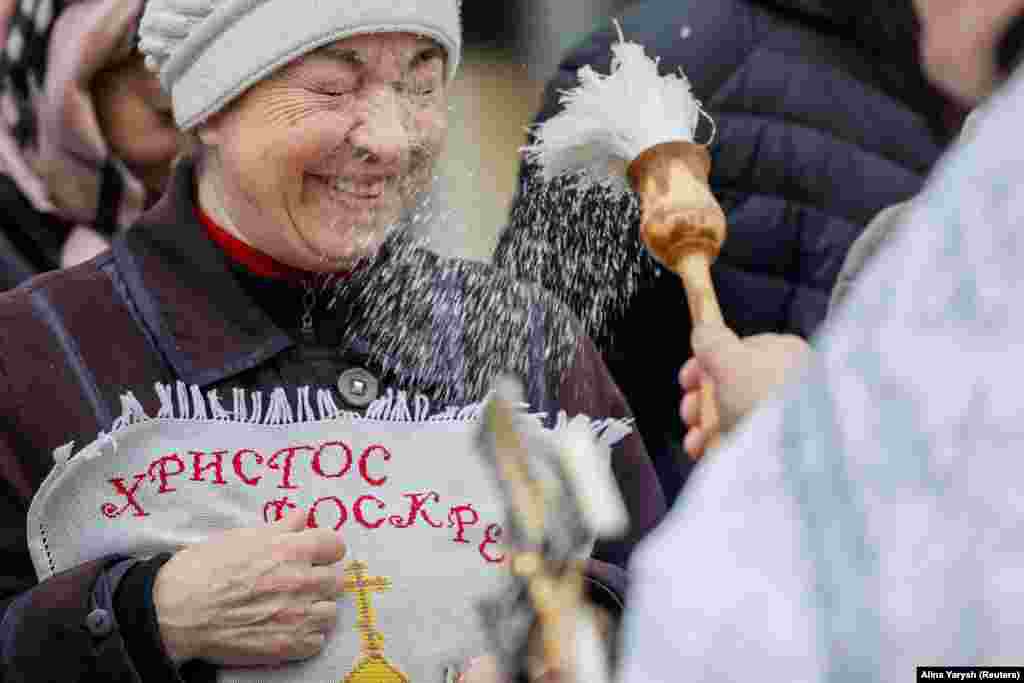 Священник окропляє свяченою водою вірянку на свято Великодня у Києві, 16 квітня 2023 року