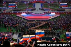 Люди слушают выступление президента России Владимира Путина (в центре сцены) во время патриотического концерта, посвящённого предстоящему Дню защитника Отечества, на стадионе «Лужники» в Москве 22 февраля 2023 года