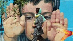 A woman walks past a wall painting of a child in Tehran.