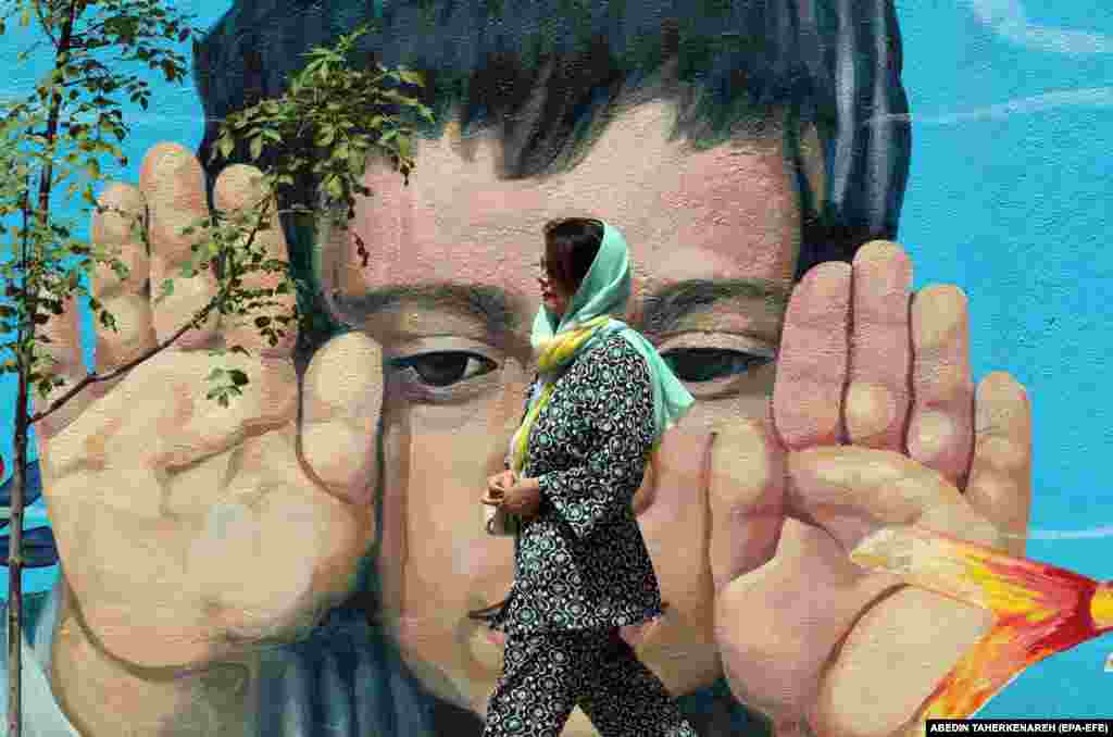 A woman walks past a wall painting of a child in Tehran.