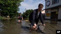 Местные жители Новой Каховки пытаются проехать на велосипедах по затопленной дороге после подрыва плотины Каховской ГЭС в ночь на 6 июня 2023 года