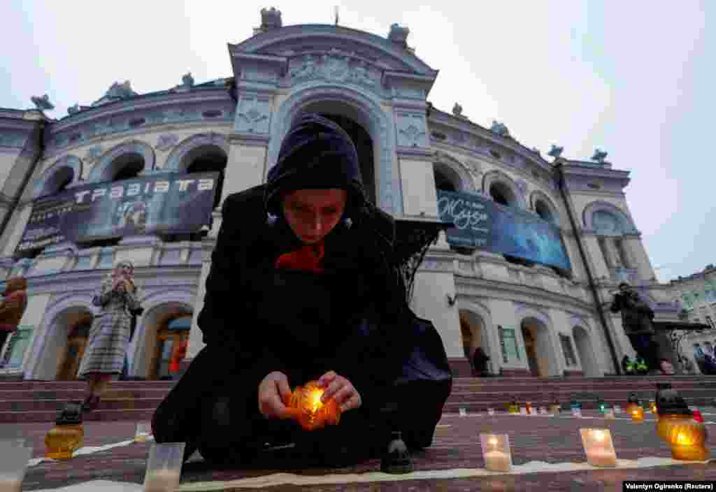 A woman lights a candle during a commemorative rally for people killed a year ago inside building of the Mariupol&#39;s Drama Theater by a Russian air strike, in front of the Opera Theater in Kyiv on March 16.