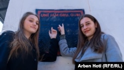 Shkëndije Behaj dhe Arbenita Bytyçi, studente, qëndrojnë para një mbishkrimi "Unë jam gru, gur" në Prishtinë. Ato nuk besojnë se mund të mbesin të papuna pas diplomimit.