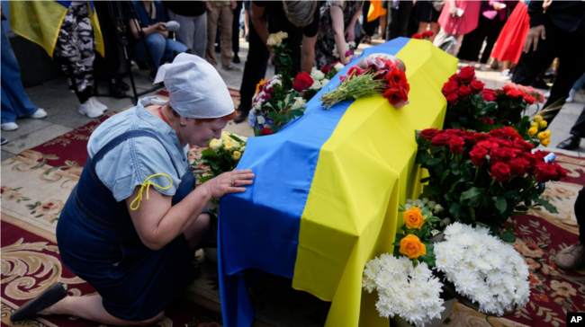 A woman kneels at the coffin of activist and soldier Roman Ratushniy during his memorial service in Kyiv on June 18, 2022.