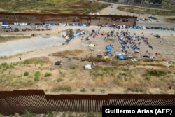 Вид сверху на мигрантов, ожидающих обработки документов властями США, между ограждениями пограничной стены на американской стороне границы США и Мексики (город Тихуана, штат Нижняя Калифорния), 11 мая 2023 года