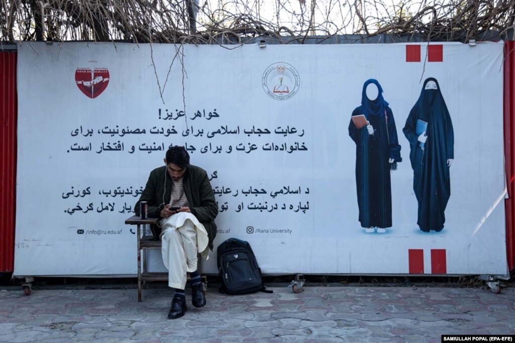 Një student i universitetit privat Rana, shihet ulur pranë një posteri me një mesazh në lidhje me kodin e veshjes për studentet femra. Universitetet në Afganistan u rihapën më 6 mars, por vetëm burrat u lejuan të ktheheshin në klasa për shkak të ndalimit të arsimit të lartë për vajzat dhe gratë nga ana e talibanëve.