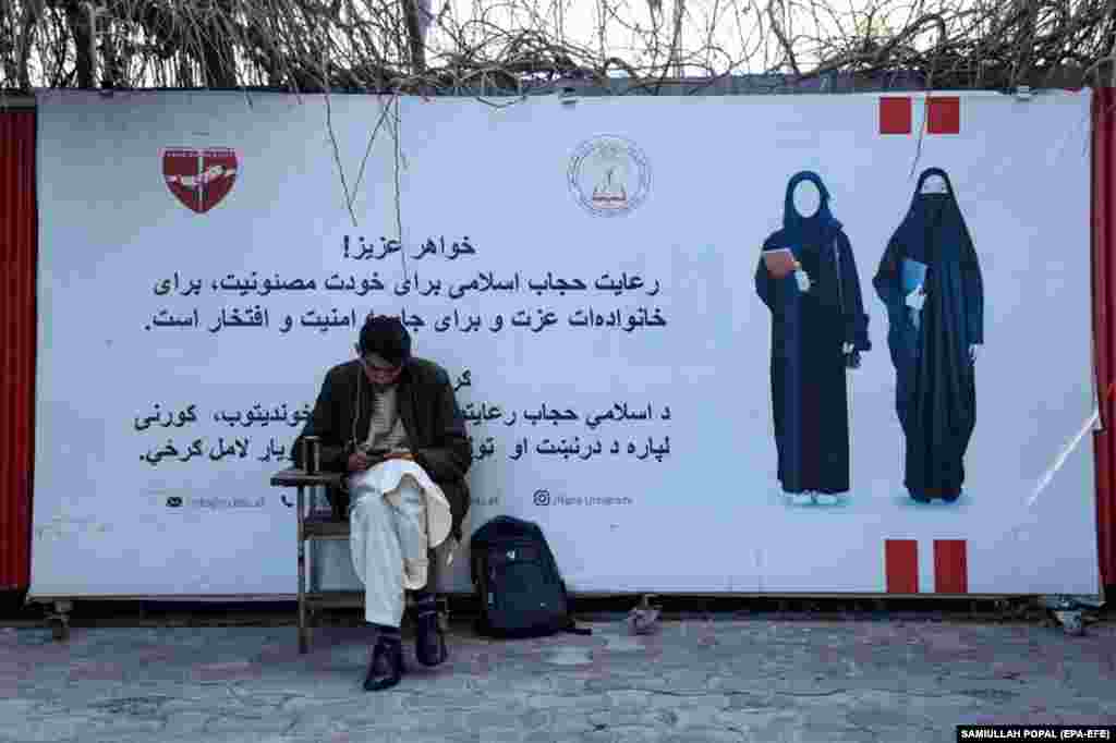 A student of the private Rana University sits beside a poster with a message about the dress code for female students. Universities in Afghanistan reopened on March 6, but only men were allowed to return to class due to a ban on women in higher education imposed by the Taliban.