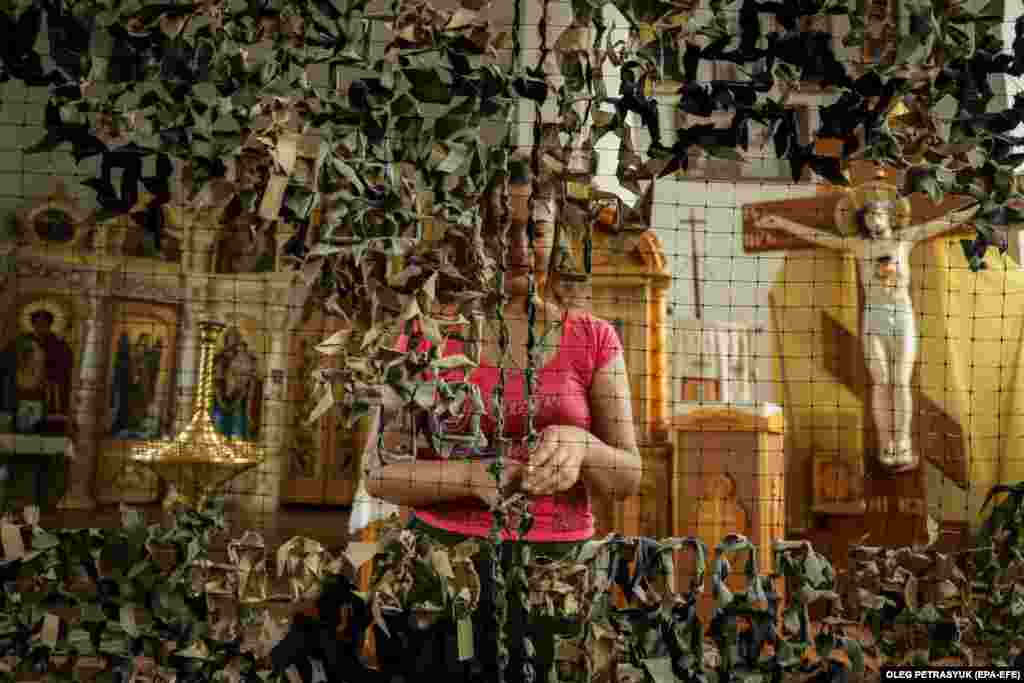 A woman weaves a camouflage net at St. Nicholas Church in Poltava, Ukraine, where church members and volunteers have gathered every day since the February 2022 Russian invasion to weave the nets for the Ukrainian Army.