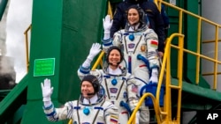  На тази фотография, оповестена от Роскосмос, астронавтът на НАСА Трейси Дайсън (в центъра), руснакът Олег Новицки и Марина Василевская от Беларус махат, до момента в който се качват на борда на галактическия транспортен съд 