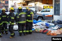 Пожарникарите стојат до покриените тела на жртвите на местото на смртоносниот пожар, во Јоханесбург