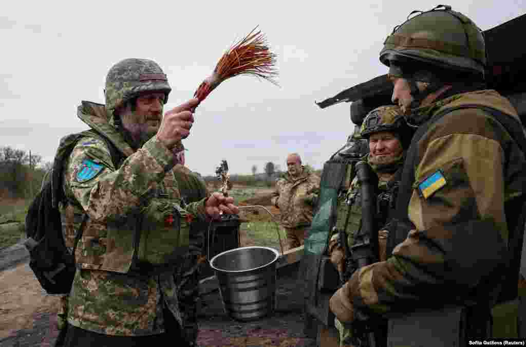 Військовий капелан Юрій на позицях ЗСУ у Харківській області кропить українських військових свяченою водою, 15 квітня 2023 року