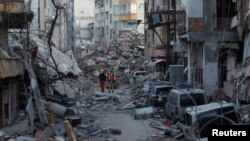Punëtorët e shpëtimit kalojnë përmes ndërtesave të shkatërruara në Hataj të Turqisë. 15 shkurt 2023. 