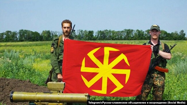 Na Telegram kanalu organizacije RUSOV objavljena je fotografija koja navodno dartira iz juna 2015. godine, na kojoj Andrej Rodionov (desno) pozira sa simbolom kolovrata (slovenska svastika) u proruskoj paravojnoj brigadi Prizrak u Lugansku