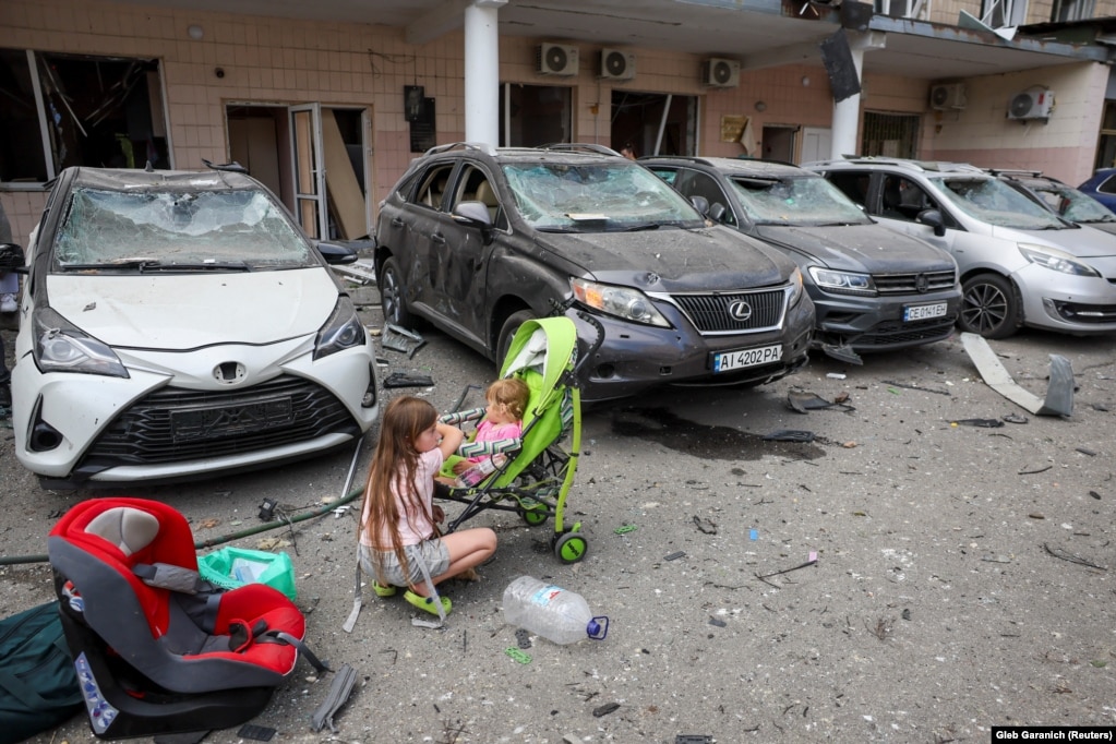 Діти біля пошкоджених російським обстрілом автомобілів та будівлі.  «Зараз з-під завалів рятувальники намагаються дістати людей. Голоси їх чують», – сказав Кличко